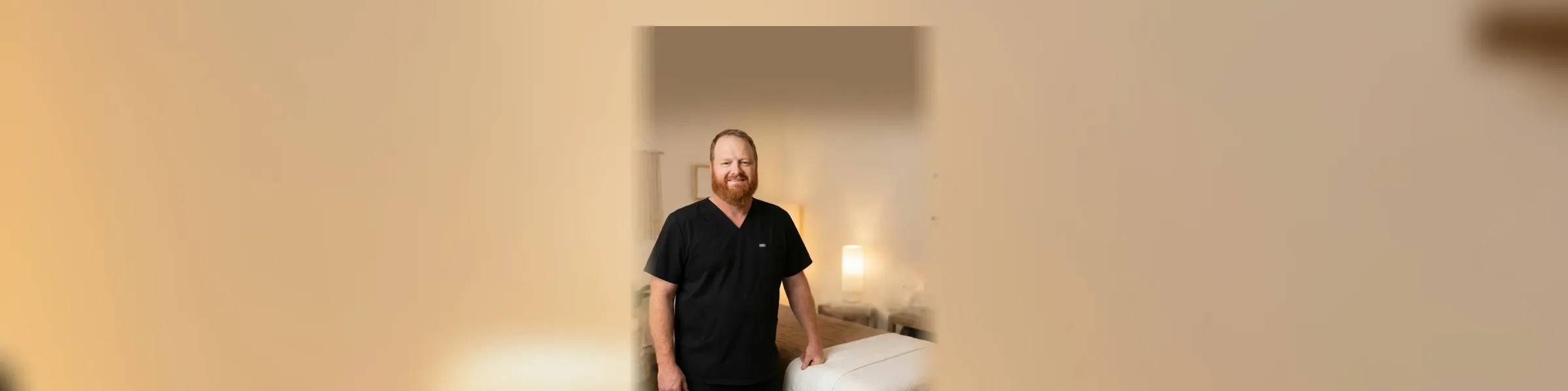 Brandon Dowacter standing beside the massage table in his warm, low-lit Princeton studio